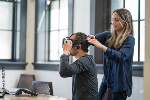 A woman helps a business colleague put on a virutal reality headset. photo