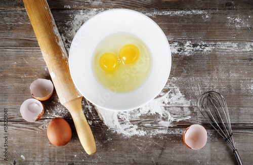 Still life with raw eggs, rolling pin and whisk on vintage wooden table background. Top view.