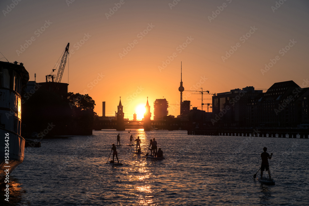 Fototapeta premium Niebo zachodzącego słońca Berlin Panorama - rzeka Spree, most Oberbaum, wieża telewizyjna i ludzie na desce do wiosłowania