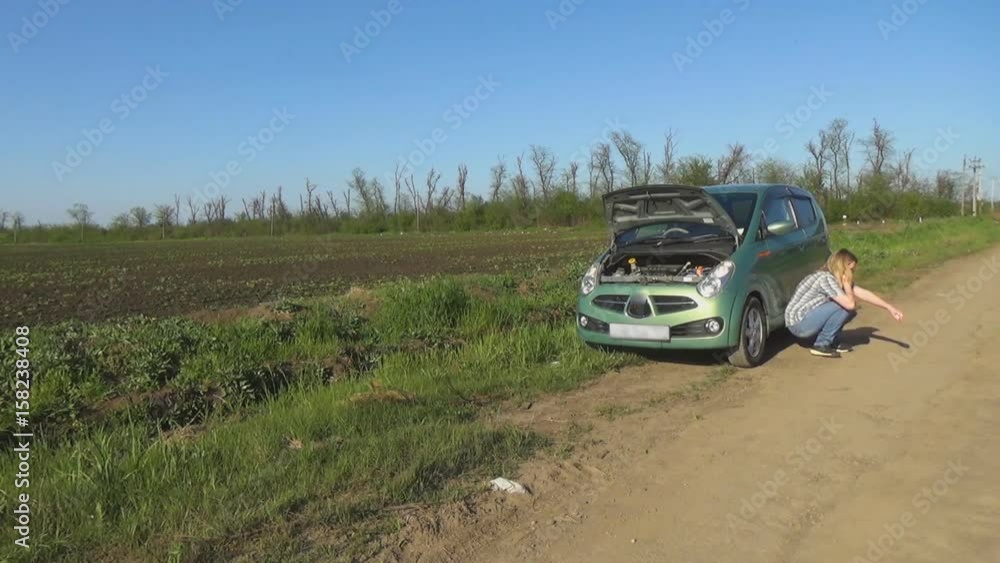 The girl is sitting on the asphalt, huddled on the car. A woman near a broken car on the track. The girl is sitting on the asphalt, huddled on the car. A woman near a broken car on the track.
