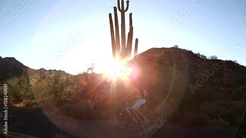 Biking in the Desert. ARIZONA, USA - May 2017. Saguaro Cactus & Bicyclist. Tilt down.  Biker at the Sonoran desert, passing the Saguaro Cactus during a golden sunset at the White Tank Regional Park we