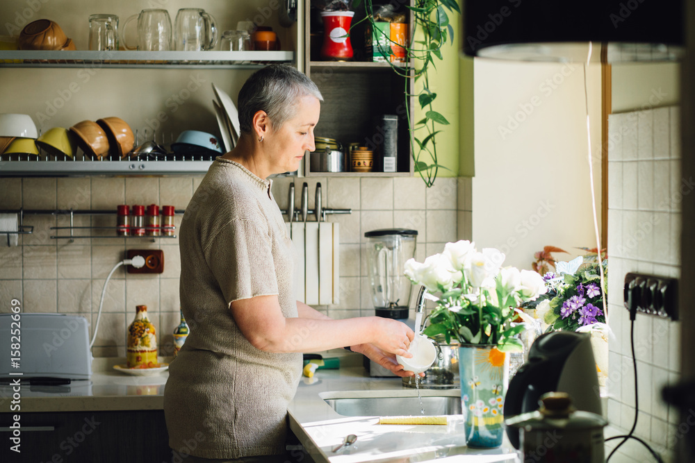 Middle age charming gray haired woman Wash dishes in the kitchen Middle age charming gray haired woman Wash dishes in the kitchen