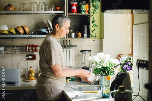 Obraz na plátně Middle age charming gray haired woman Wash dishes in the kitchen