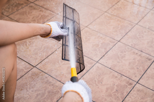 Person spraying water onto air conditioner filter to clean dust