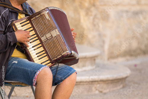 Фотография Matera, Italy - May 20, 2017: Street musician plays an old accordion sitting