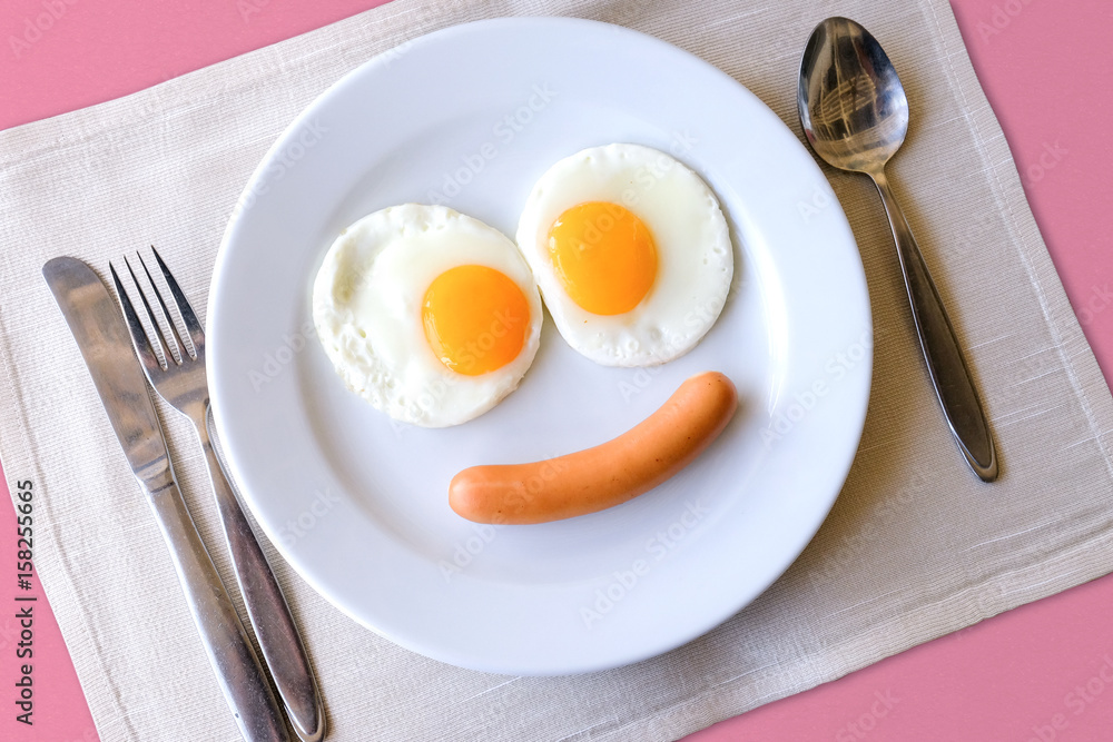 Smiling face frying eggs breakfast on a white plate background with spoon,knife and fork on a fabric table, breakfast serve for kid. Smiling face frying eggs breakfast on a white plate background with spoon,knife and fork on a fabric table, breakfast serve for kid.