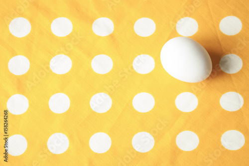 An egg on bright yellow dotted cloth. Minimal.