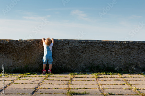 The little girl tries to see what's behind the wall.