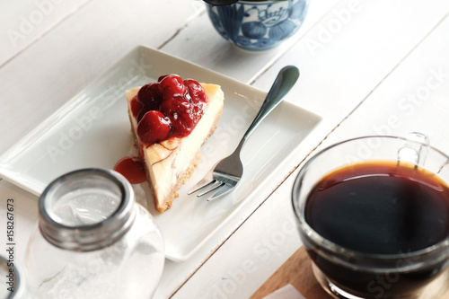 фотографія A piece of cherry cheesecake and black coffee on white wooden table