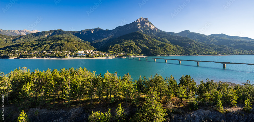 Summer panoramic view of Serre-Poncon Lake with Savines-le-Lac, its bridge and the Grand Morgon mountain peak. Hautes-Alpes, PACA Region, Southern French Alps, France