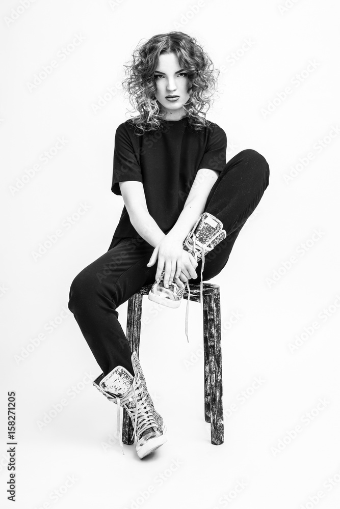Fototapeta premium A smart girl is sitting on a chair in a fashionable suit. Black white photo of a girl.