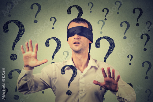 blindfolded man stretching his arms out walking through many question marks