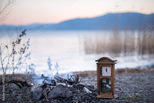 burning branches and old wooden wall clock on a beach of a lake prespa in macedonia