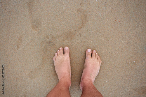 men's feet on the sand. top view of male feet on a sandy beach with footprints