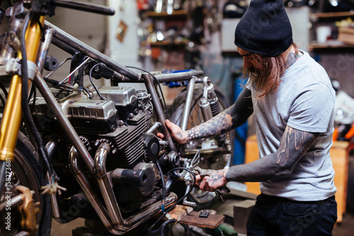 Portrait of focused tattooed man working in garage customizing motorcycle and repairing broken parts photo