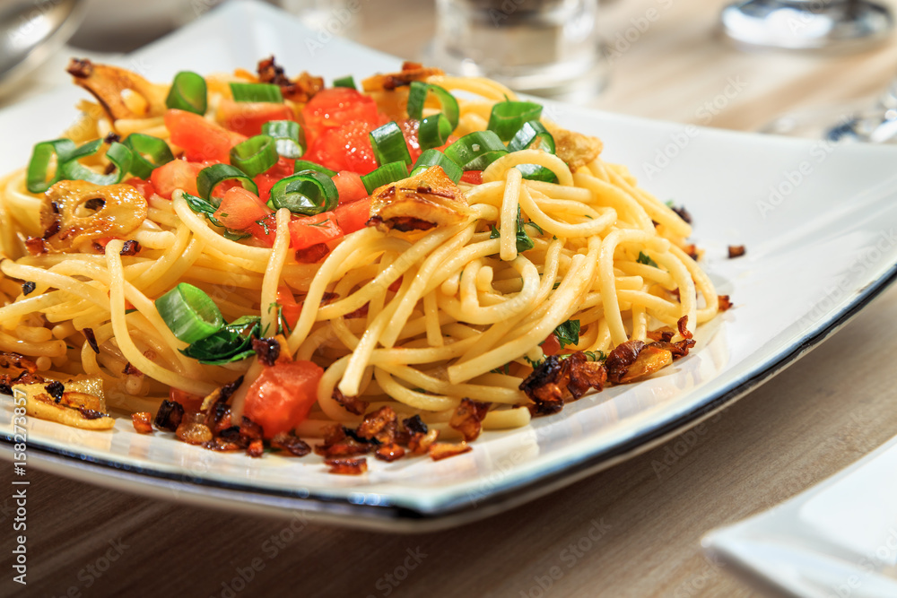 spaghetti with tomatoes, roasted garlic and green onions on a beautiful rectangular plate are on the table