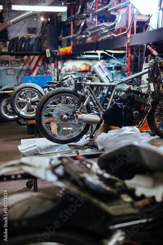 Back view portrait of tattooed man working in garage repairing motorcycles