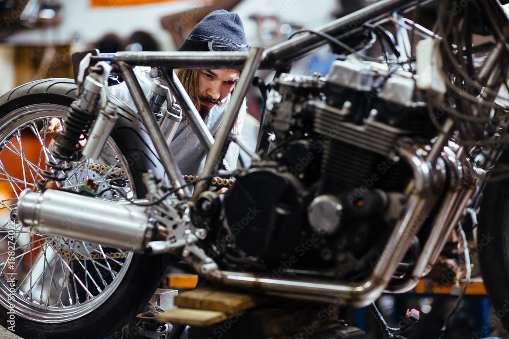 Portrait of bearded long-haired man working in garage customizing  motorcycle and repairing broken parts