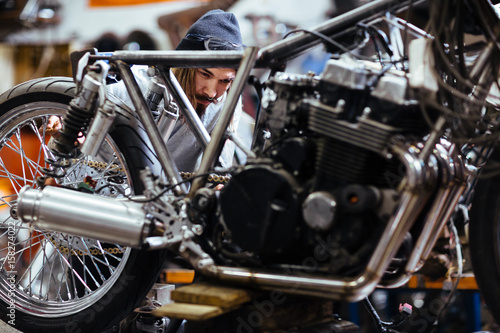 Portrait of bearded long-haired man working in garage customizing  motorcycle and repairing broken parts © pressmaster