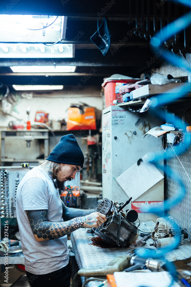 Side view portrait of modern tattooed man fixing broken engine in workshop Side view portrait of modern tattooed man fixing broken engine in workshop