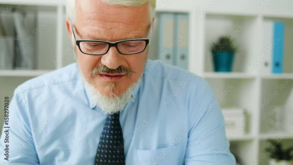 Portrait of caucasian middle aged man with glasses in blue shirt at his office. Business man thinking about something, smiling. Close up Portrait of caucasian middle aged man with glasses in blue shirt at his office. Business man thinking about something, smiling. Close up