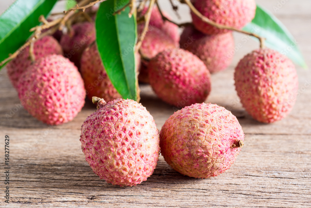 close up of chinese litchi (lichee, lychee) and bunch at back on old wood (Litchi chinensis Sonn., Sapindaceae)