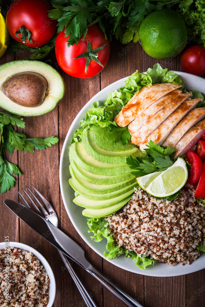Plakat Healthy salad bowl with quinoa, tomatoes, chicken, avocado, lime and mixed greens (lettuce, parsley) on wooden background top view. Food and health.