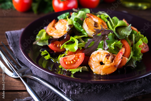 Fresh salad plate with shrimp, tomato and mixed greens (arugula, mesclun, mache) on wooden background close up. Healthy food. Clean eating.