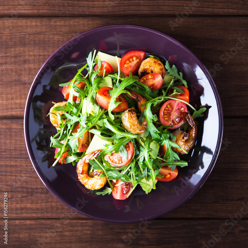 Fresh salad plate with shrimp, tomato, avocado and arugula (salad rocket) on wooden background top view. Healthy food. Clean eating.
