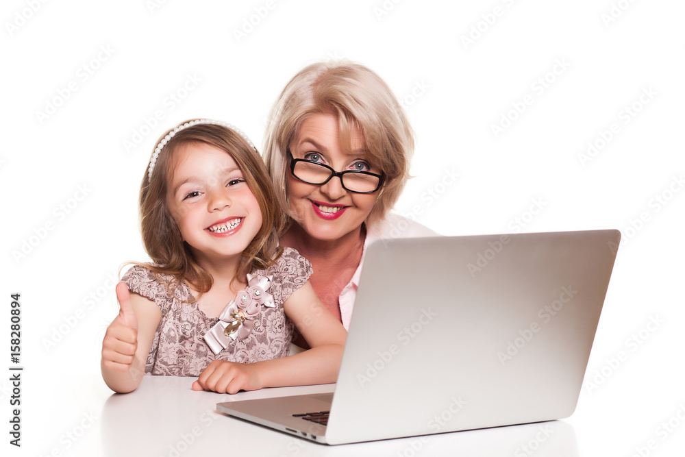 Grandmother and her granddaughter sitting at the table and using laptop on white background