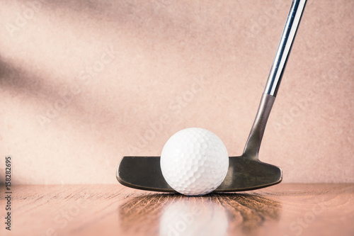 still life photography : golf club (putter) and ball on wood table against brown wall with window light at left