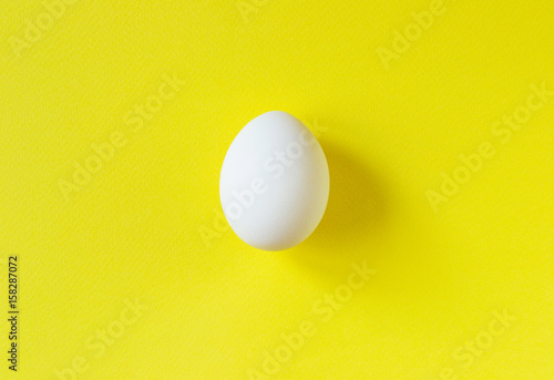 Single white egg on vibrant yellow background