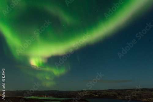 The Aurora in the sky above the hills and water on a moonlit night. © Moroshka
