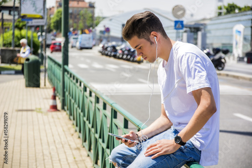 Close up of Young Man Listening to his Favorite Music Using Earphone in City Environment, Using MP3 Player or Smartphone