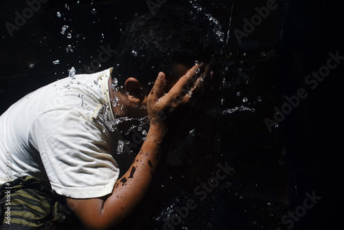 Man Washing The Face With Flowing Clear Water In Dramatic Light Over Black Background