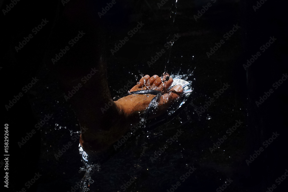 Fototapeta premium Wash The Feet With Flowing Clear Water In Dramatic Light Over Black Background