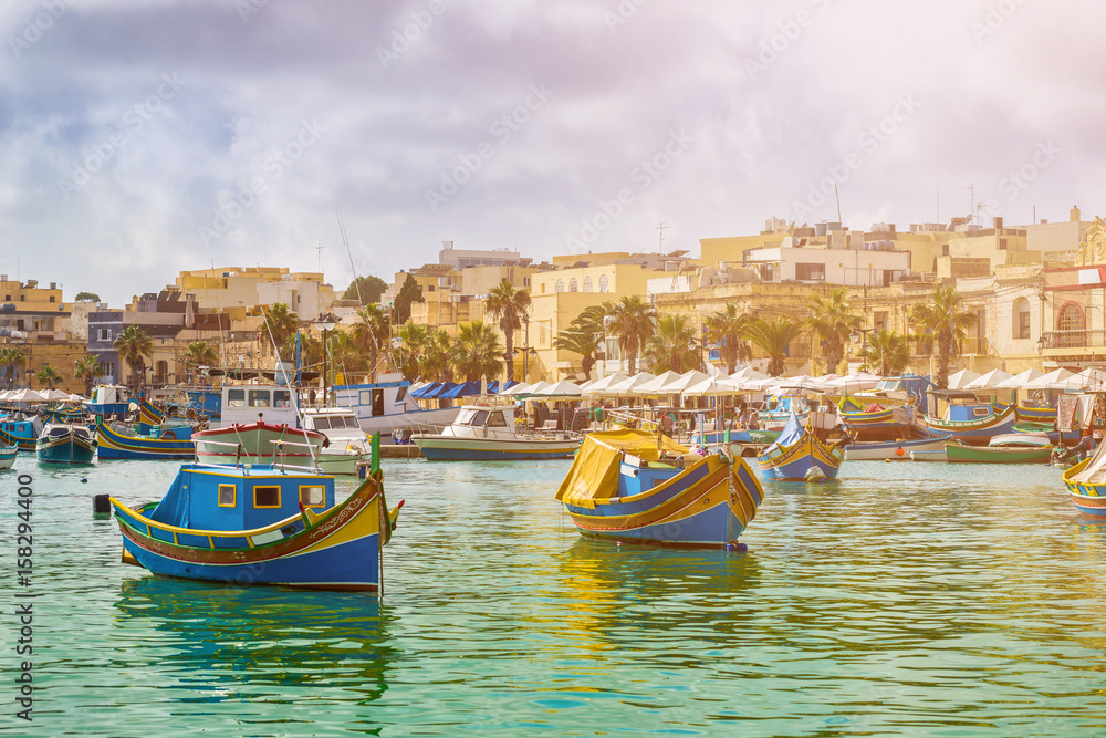 Marsaxlokk, Malta - Traditional colorful maltese Luzzu fisherboats at the old village of Marsaxlokk with turquoise sea water and palm trees on a summer day Marsaxlokk, Malta - Traditional colorful maltese Luzzu fisherboats at the old village of Marsaxlokk with turquoise sea water and palm trees on a summer day