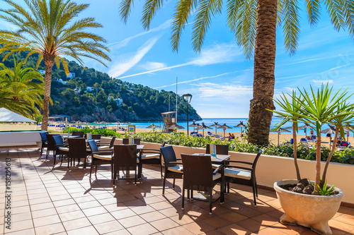 Bar tables terrace on beach with palm trees in Cala San Vicente bay, Ibiza island, Spain photo