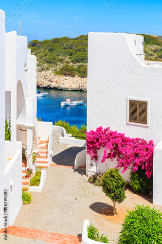Obraz na płótnie Traditional white houses decorated with flowers and view of fishing boat on sea in Cala Portinatx bay, Ibiza island, Spain w salonie