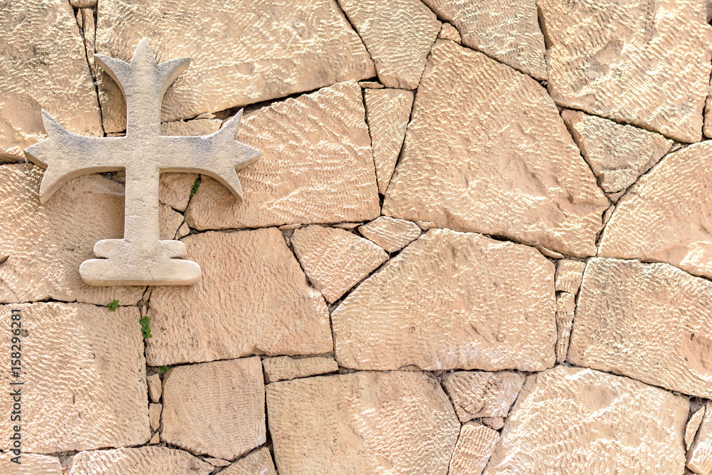 Stone cross hanging on a stone wall, background