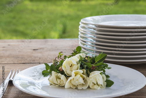 summer table setting with white wild rose flowers on rustic wooden table outdoors