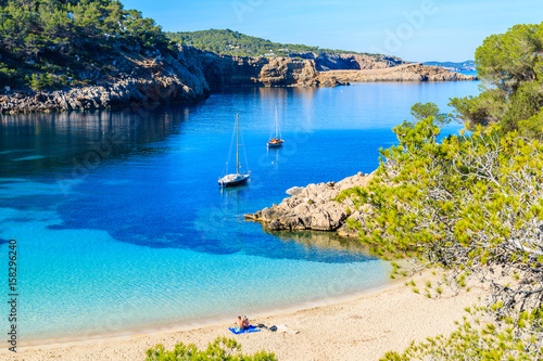 Couple of unidentifed people sunbathing on beautiful beach in Cala Salada famous for its azure crystal clear sea water, Ibiza island, Spain