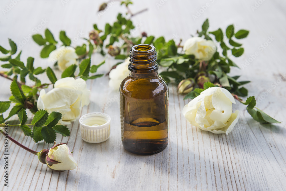 vial with essential oil from wild rose flowers on light wooden background vial with essential oil from wild rose flowers on light wooden background