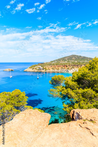 View of Cala d'Hort bay with beautiful azure blue sea water and pine trees on cliff rocks, Ibiza island, Spain