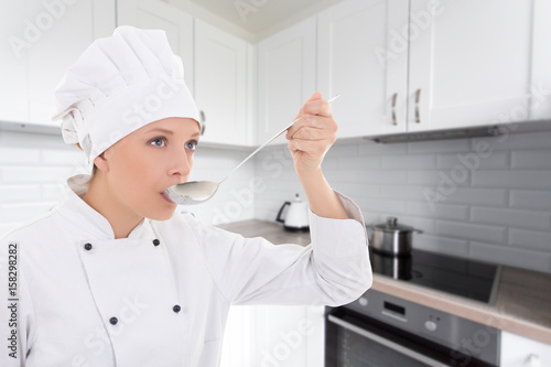 young woman in chef uniform tasting something in kitchen