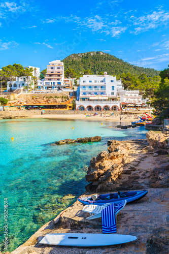 Kayak and dinghy boat on sea shore and view of hotels in Cala Portinatx bay, Ibiza island, Spain photo