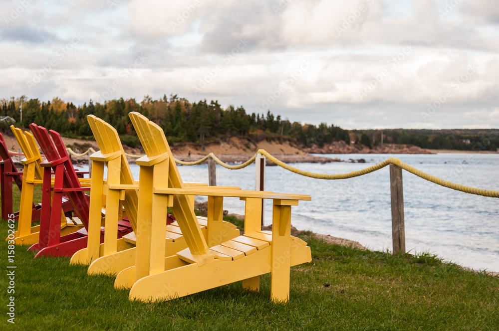 a row of yellow and red adironack chair overlooking water a row of yellow and red adironack chair overlooking water
