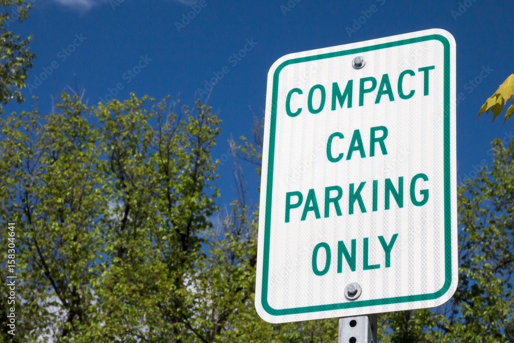 Compact car parking only sign against sky and green treetops