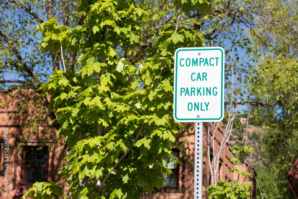 Compact car parking only sign with green leaves and a building
