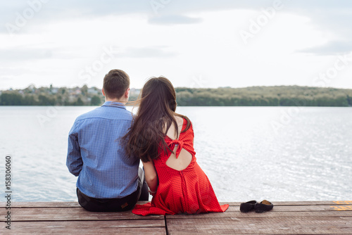 couple sitting on the beach, pier, and admire the sunset